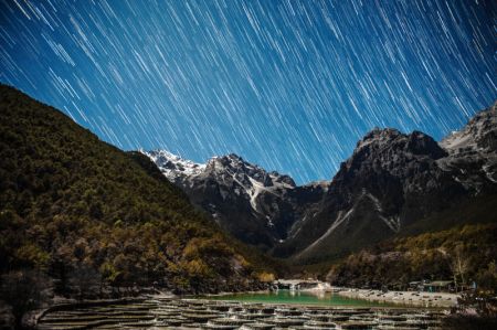 (miniature) Image obtenue en empilant plusieurs expositions montrant des traînées d'étoiles au-dessus de la montagne enneigée de Yulong