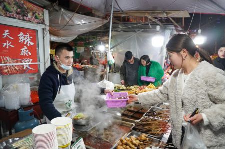 (miniature) Un propriétaire d'un stand de malatang sert une consommatrice dans une rue de snacks
