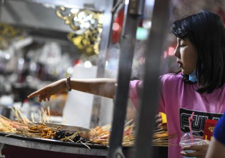 (miniature) Une touriste achète des snacks dans un marché de nuit à Hotan