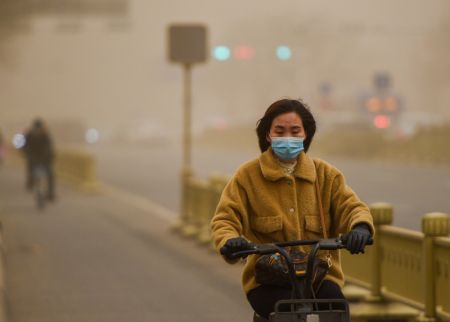 (miniature) Une femme portant un masque roule à vélo au milieu de la poussière à Hohhot