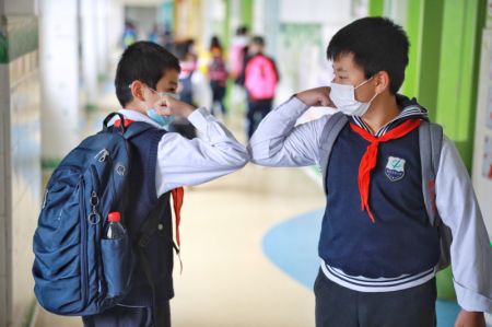 (miniature) Deux élèves se saluent en se touchant les coudes dans une école primaire de Guiyang