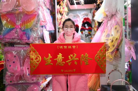 (miniature) Une commerçante montre une bannière sur laquelle est écrit activités commerciales en plein essor au marché du commerce international de la ville de Yiwu
